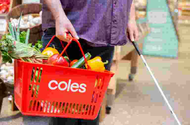 A person with a shopping basket filled with fresh produce. In their other hand is a white cane.
